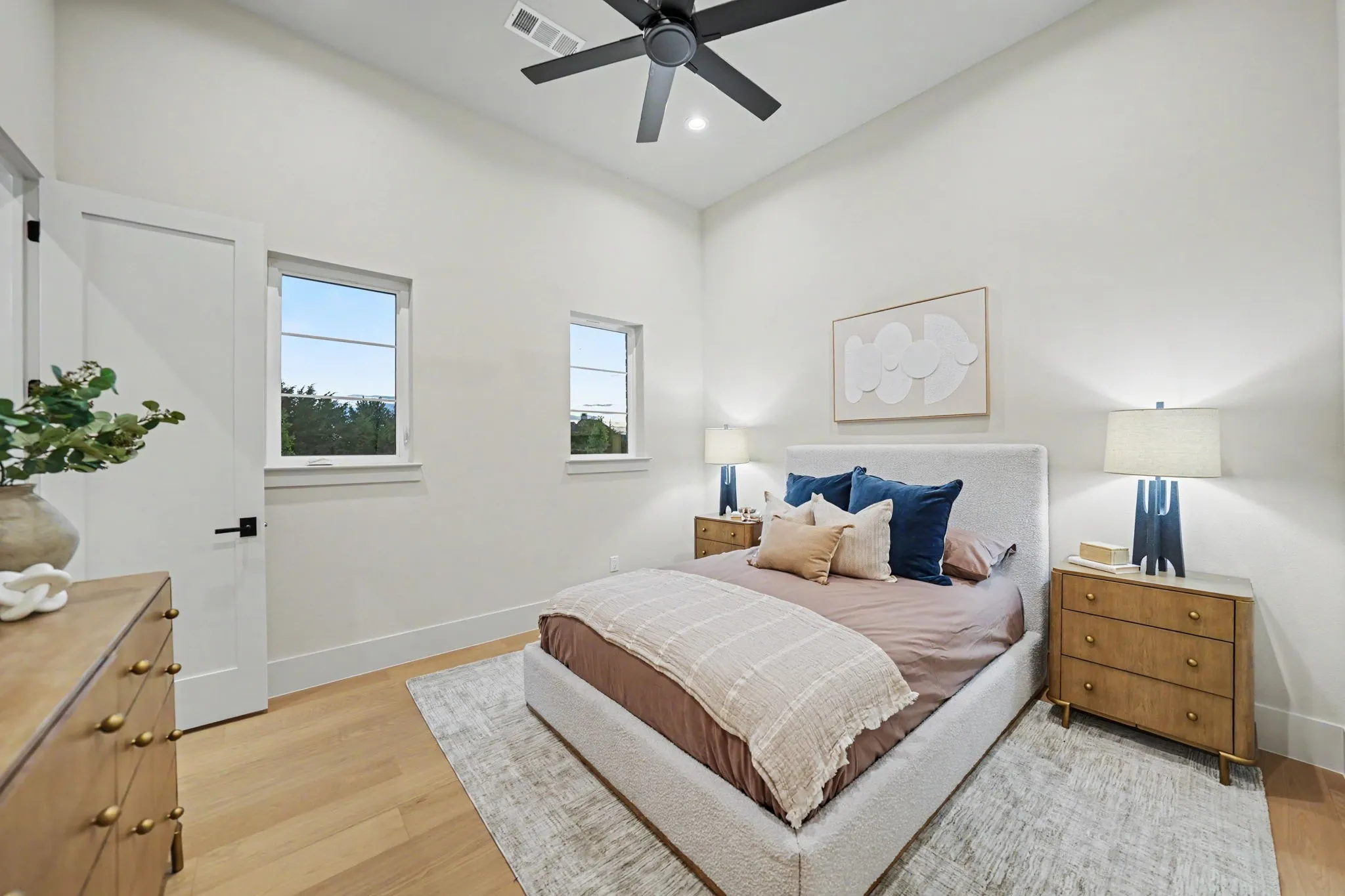 Vaulted ceiling with a ceiling fan, light wood-finish flooring, and multiple windows