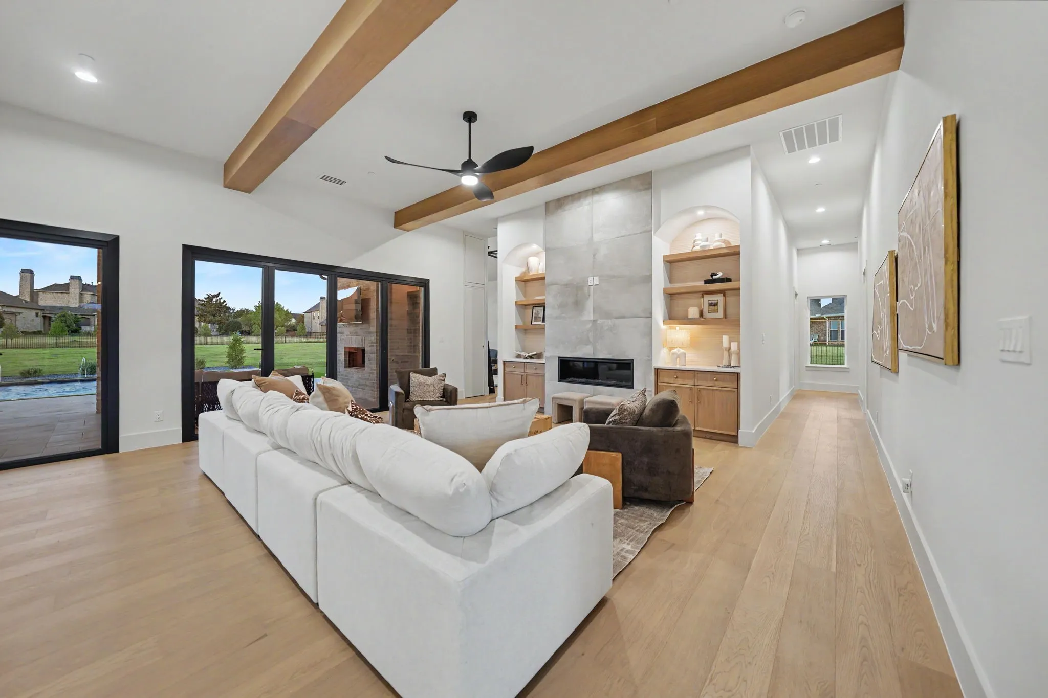 Vaulted ceiling with exposed wood beams, wood-finish flooring, built-in fireplace with concrete-look surround, custom built-in cabinetry with shelving, and large exterior glass doors