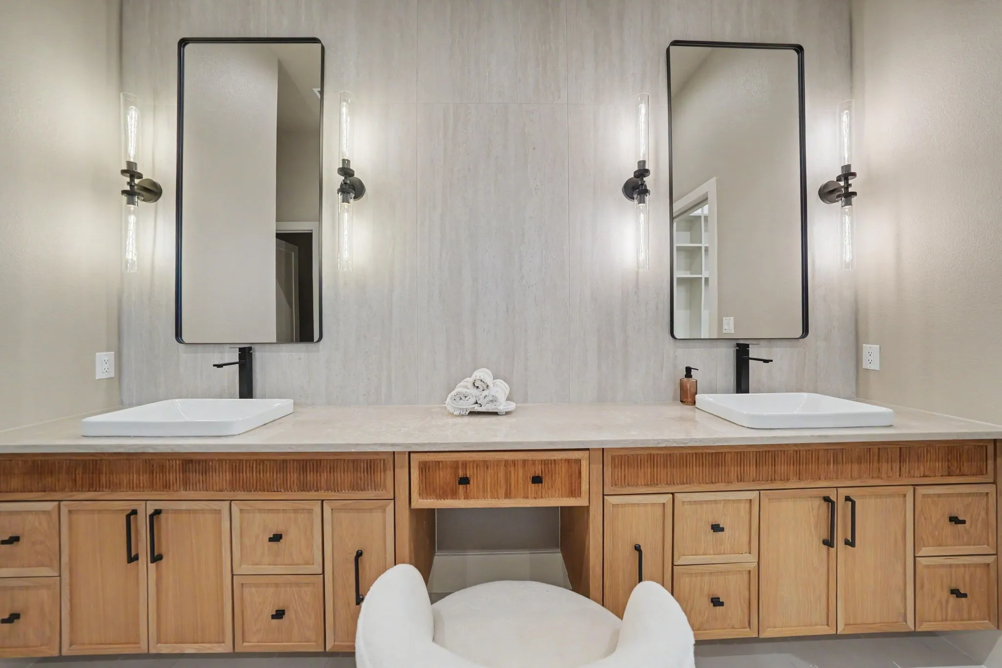 Dual vanity with vessel sinks, black framed mirrors, wall-mounted light fixtures, and wood-finish cabinetry