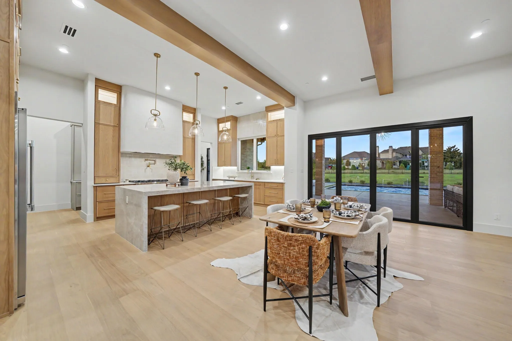 Spacious open-concept kitchen featuring light wood-finish cabinetry, a large center island with countertop seating, recessed lighting, and exposed ceiling beams