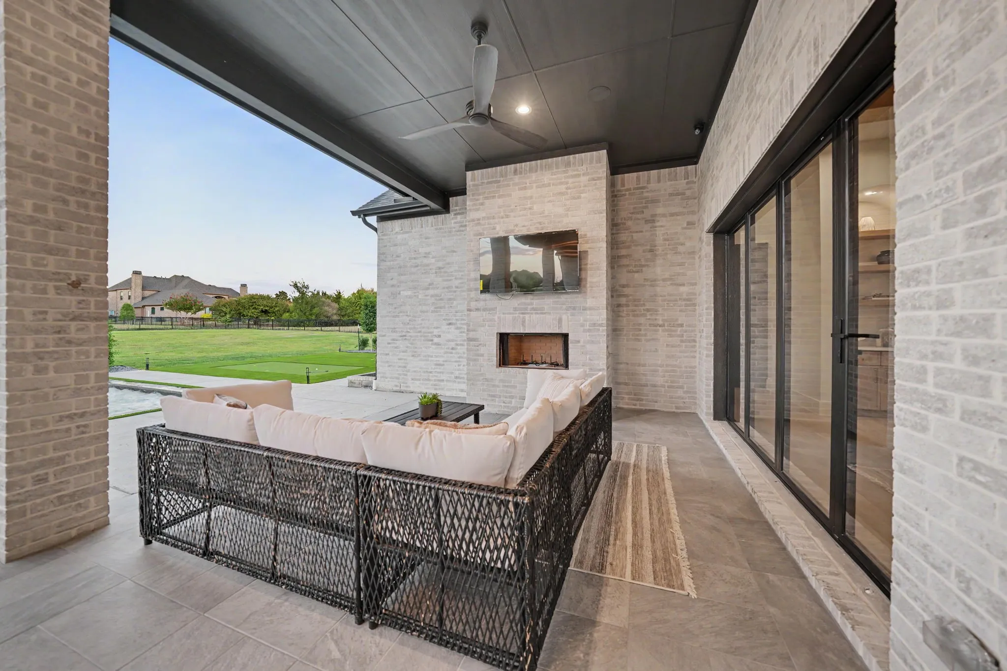 Covered patio featuring a brick fireplace, ceiling fan, and large sliding glass doors