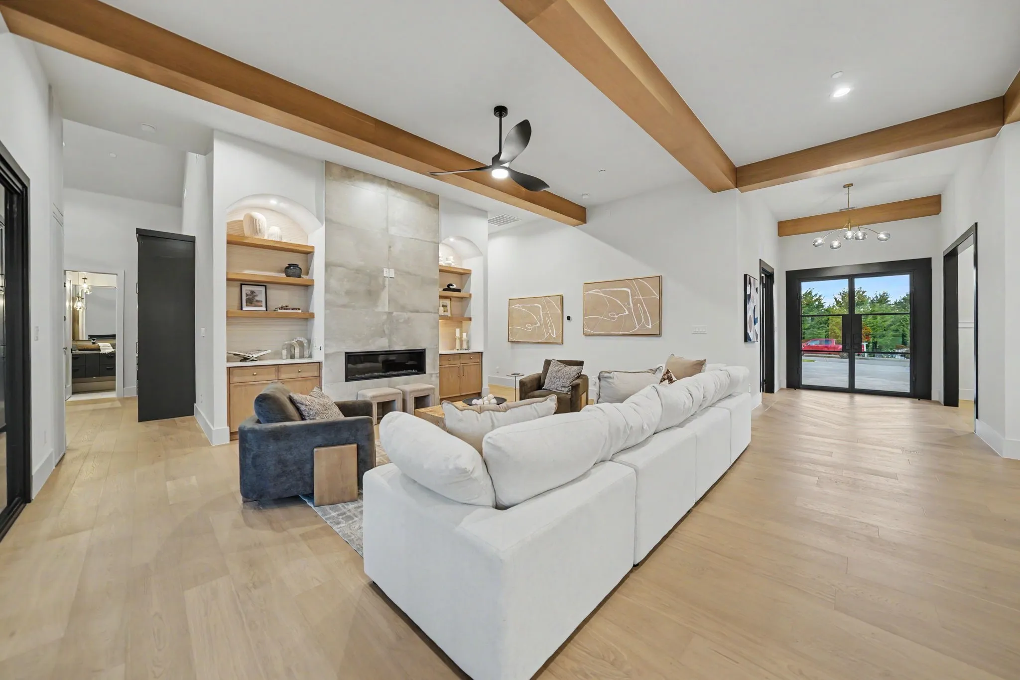 High vaulted ceilings with exposed wood beams, a modern fireplace with stone-finish surround, built-in shelving with integrated lighting, wood-finish flooring, and black-framed French doors
