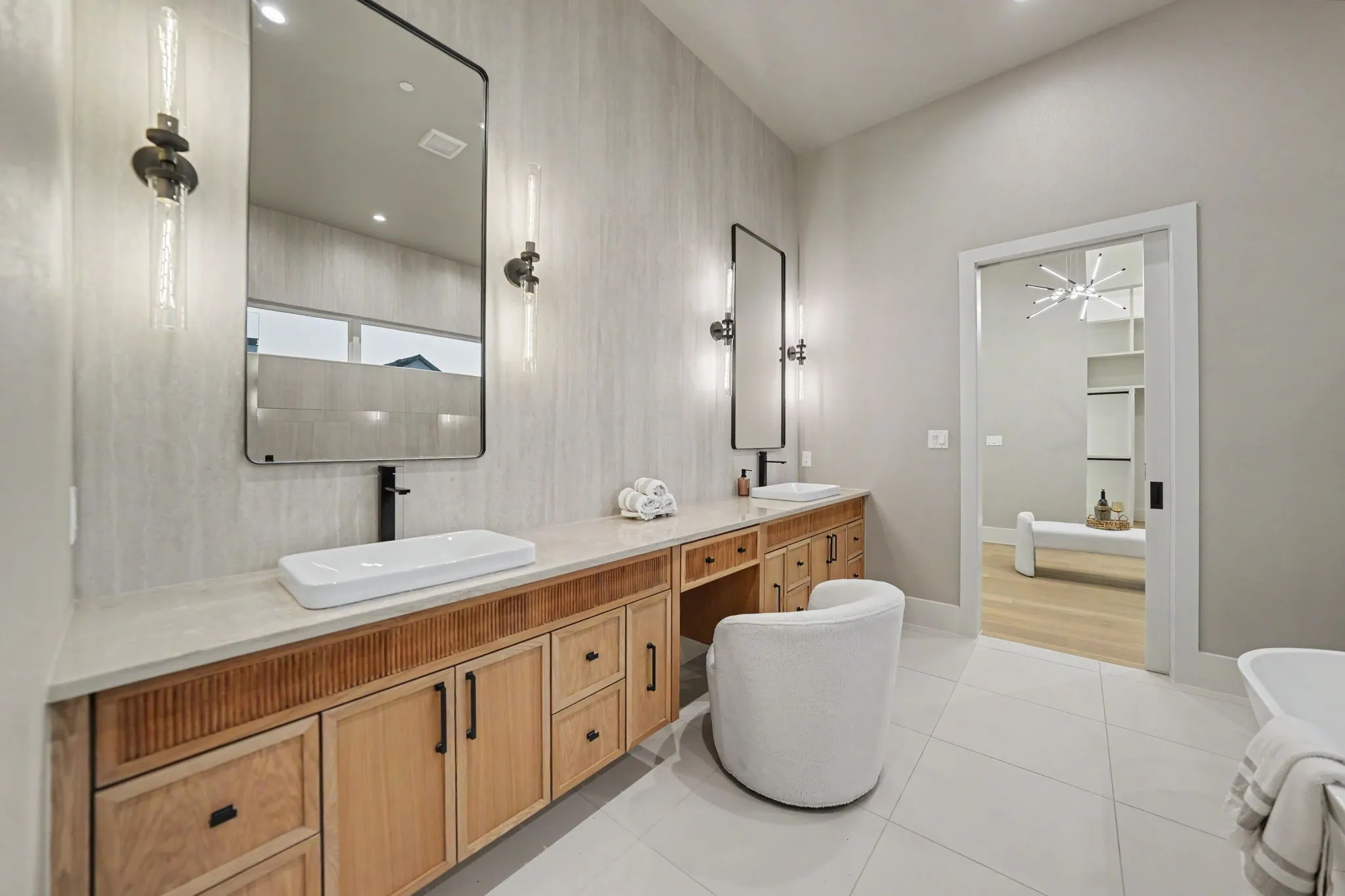 Dual wall-mounted mirrors with integrated lighting, wood-finish vanity with ample storage, dual vessel sinks, and white tile flooring