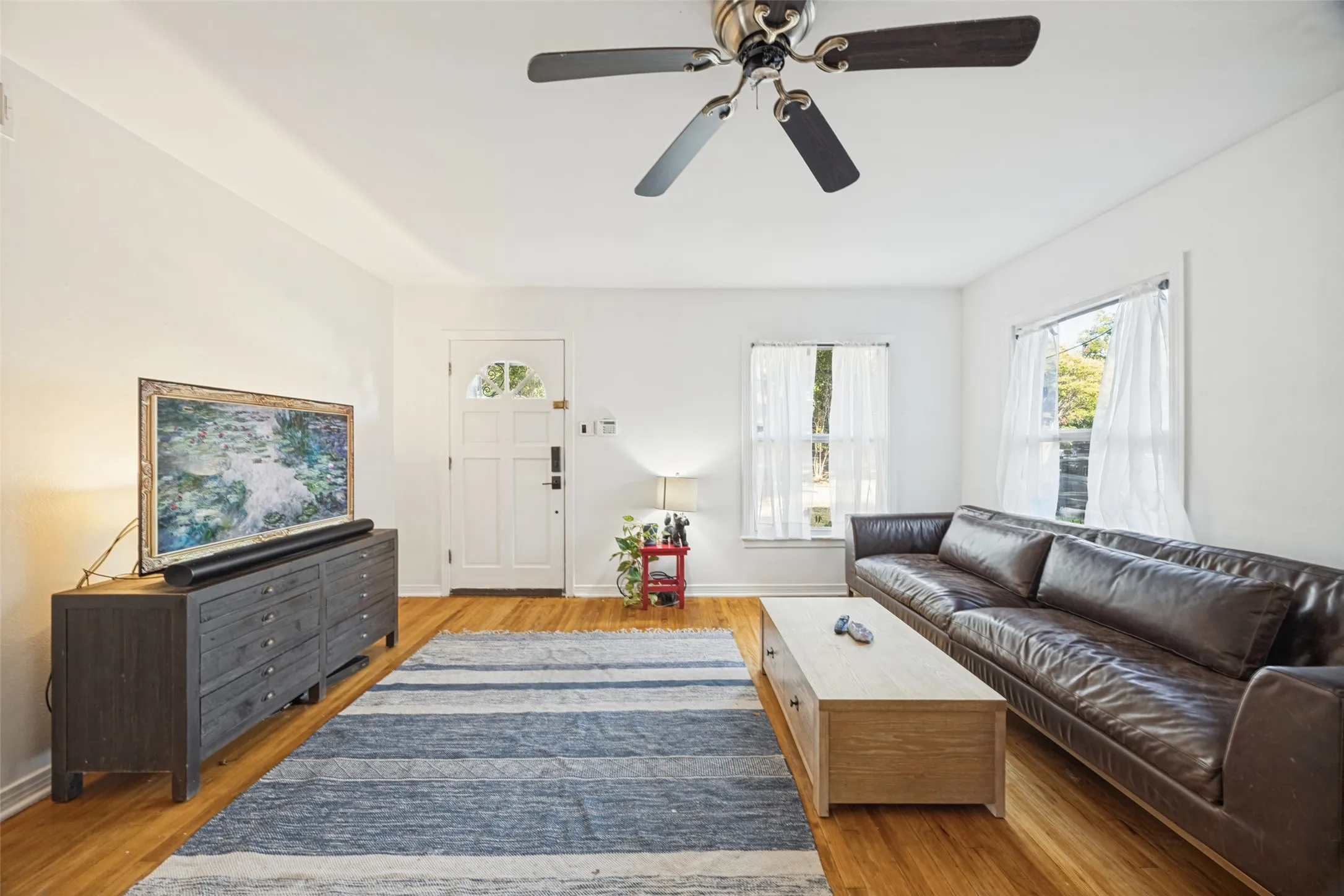 Original Hard wood flooring, fresh paint, ceiling fan, and white-paneled front door with an arched window