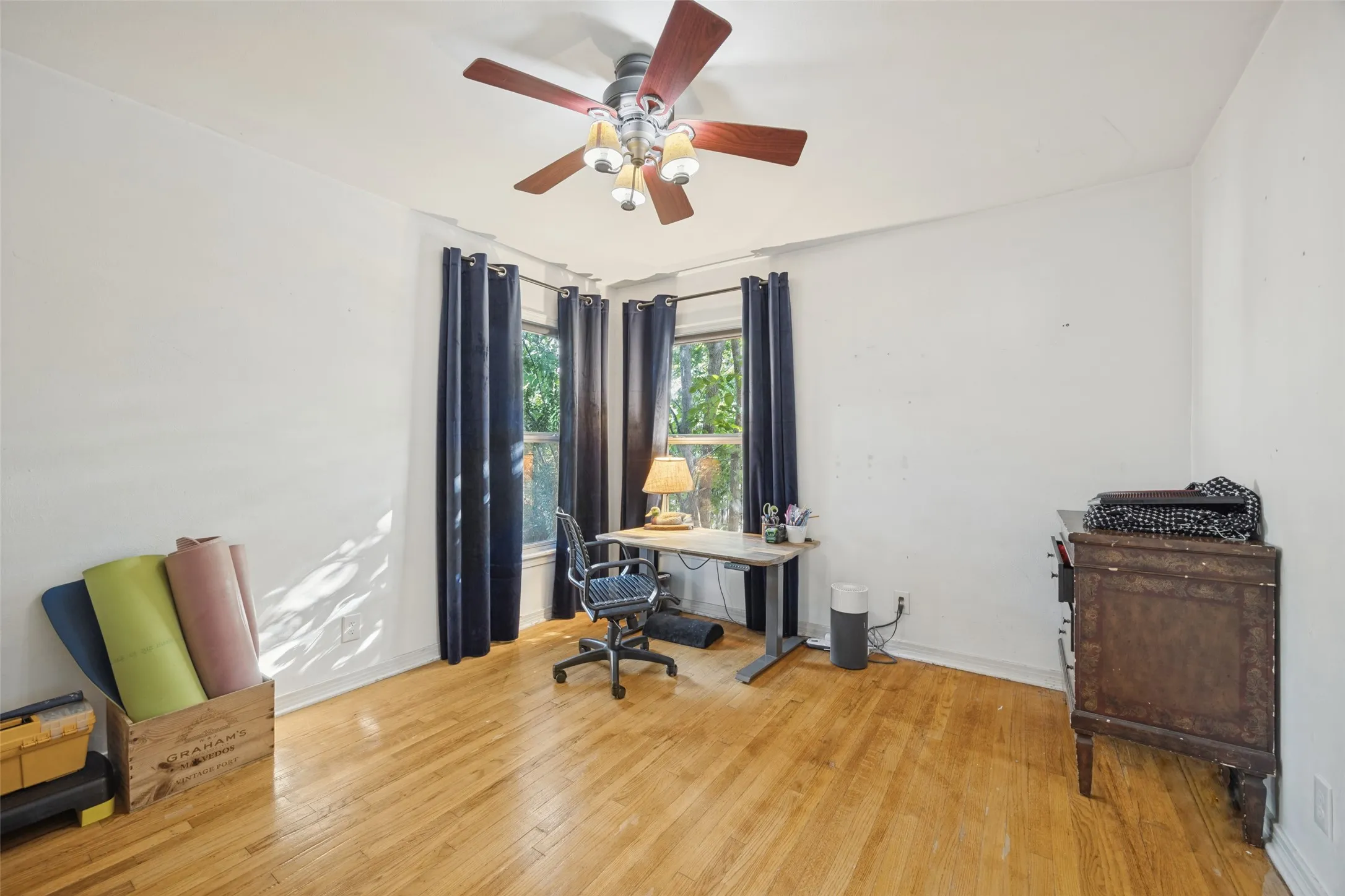 Hardwood flooring throughout, featuring a ceiling fan with integrated lighting, and multiple windows