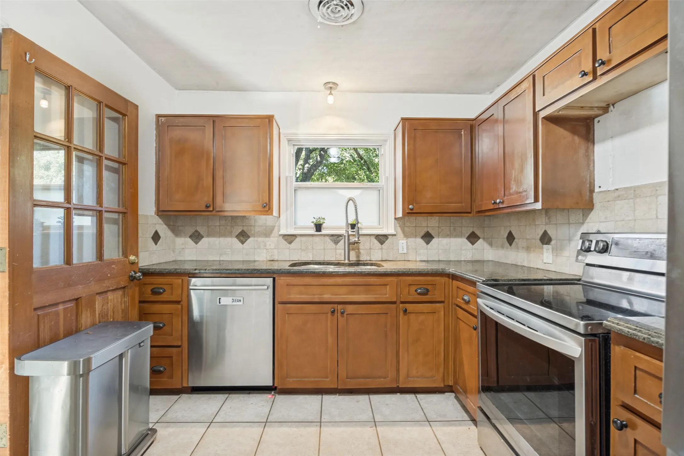Kitchen featuring wood cabinetry, SS appliances, plumbed for gas, electric induction cooktop, convection oven, and regular oven all in one, granite-style countertops, tile flooring, and tumbled marble backsplash