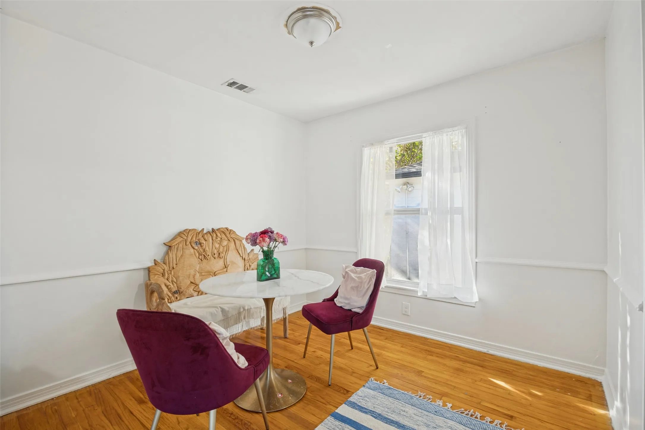 Hardwood flooring, natural light through a single window, white walls, decorative wall trim, and a ceiling-mounted light fixture
