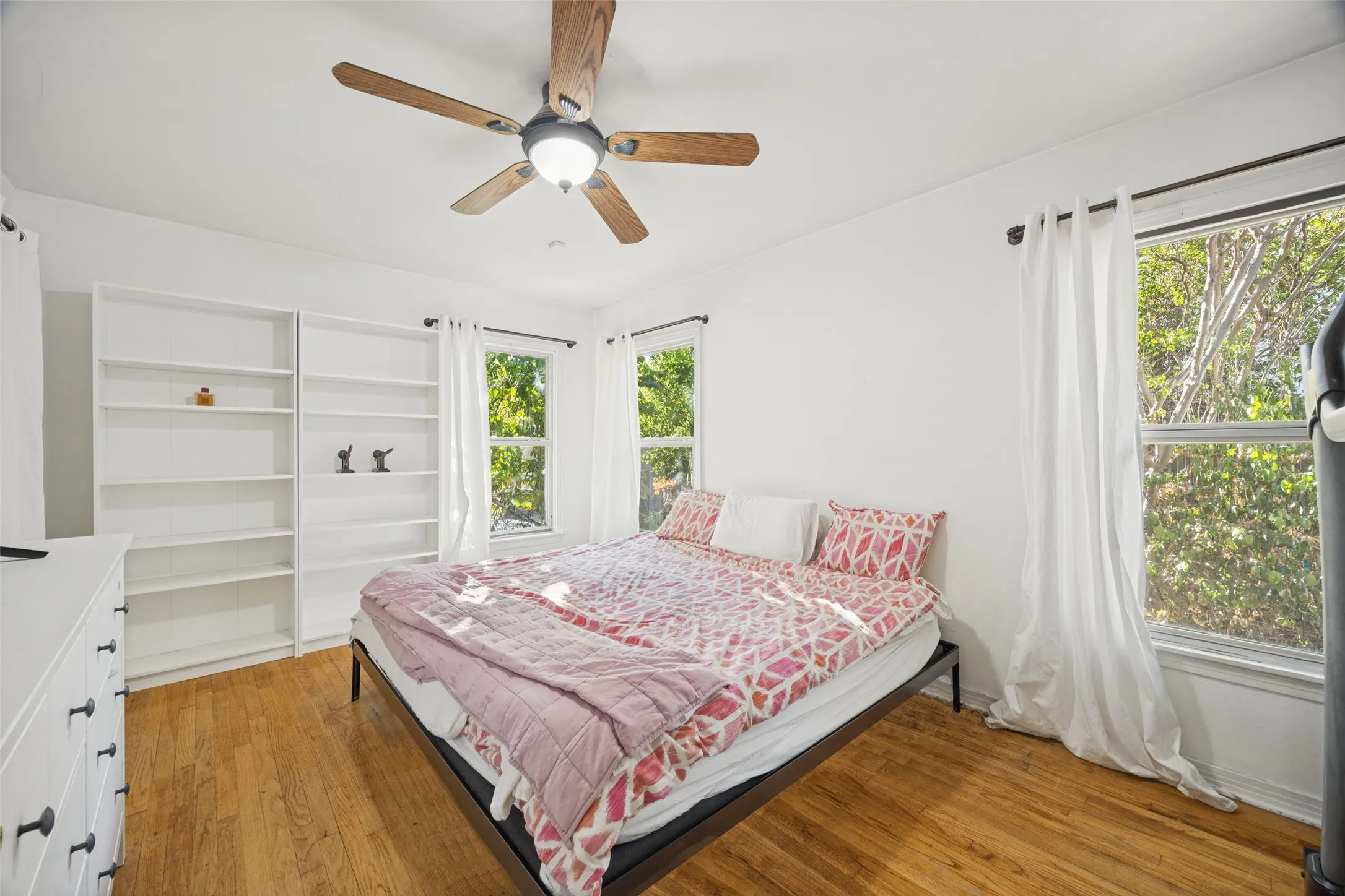 Hardwood flooring , a ceiling fan with integrated lighting, two windows, and built-in shelving