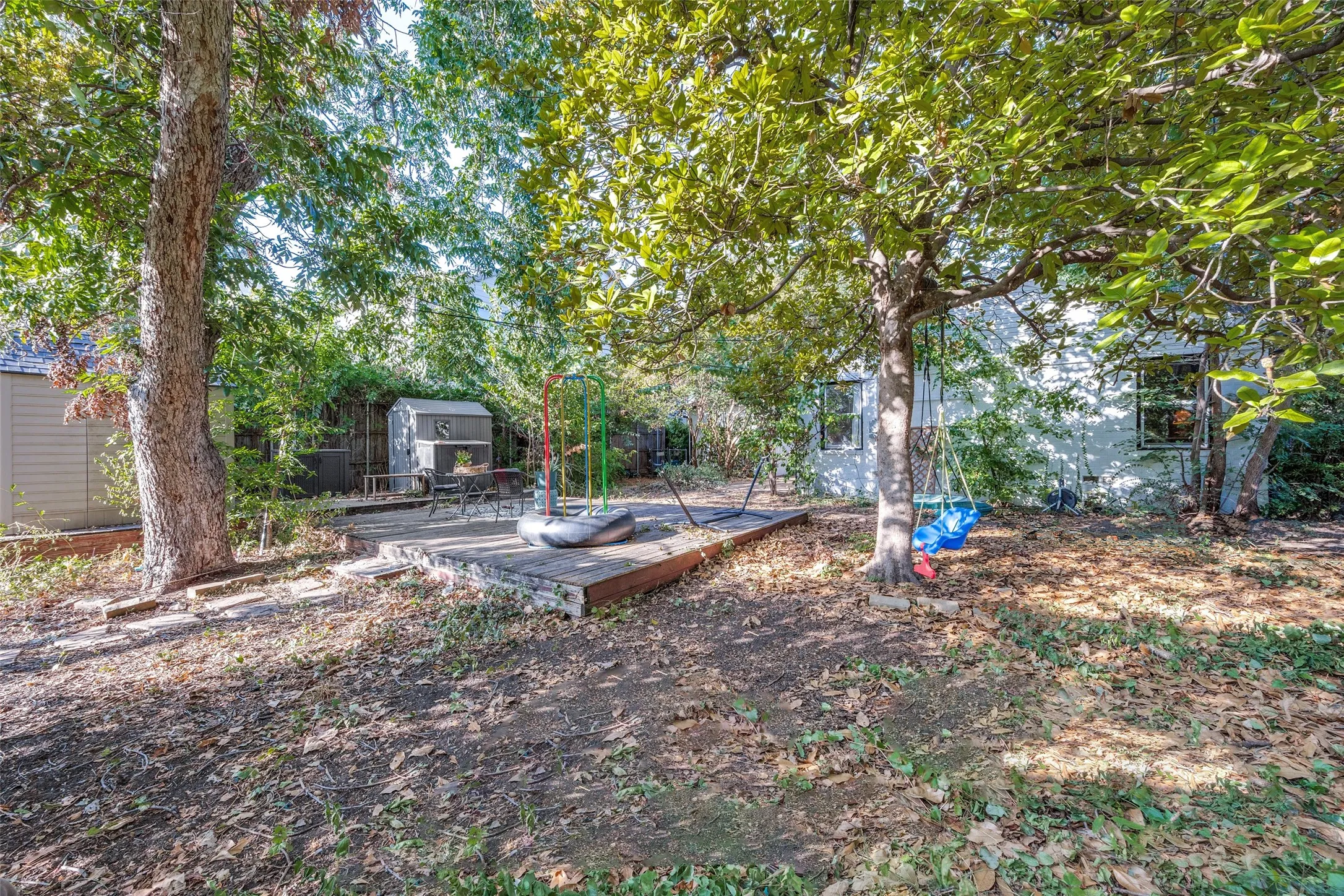 Expansive backyard featuring mature trees, a wooden patio, and two storage sheds
