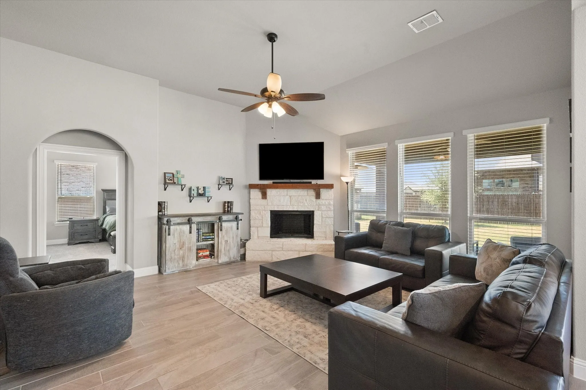Living room with wall of windows and stone fireplace. Entry to the left of the fireplace is the primary bedroom
