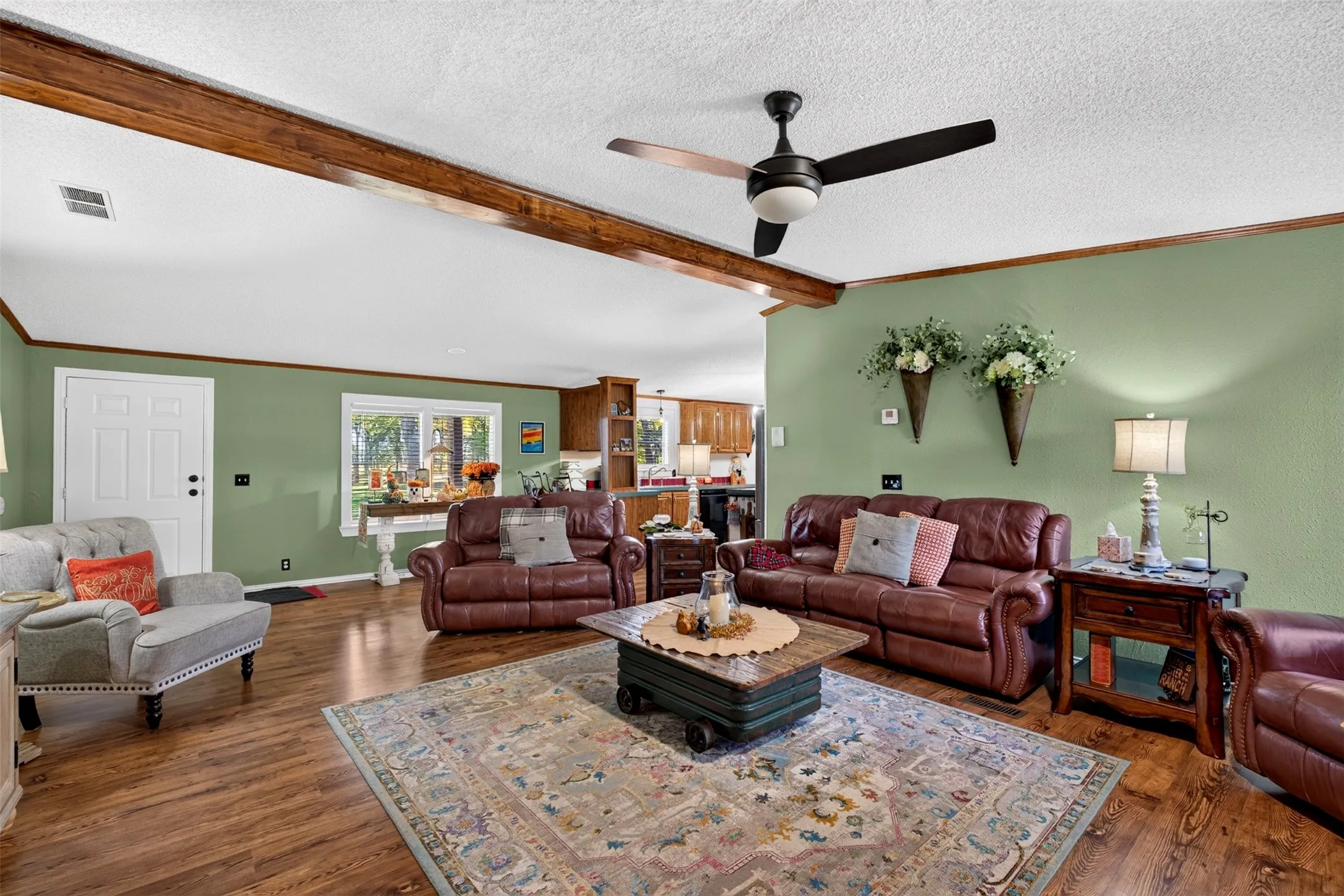 enter into spacious living room with wood beam, ceiling fan and white panel front door.