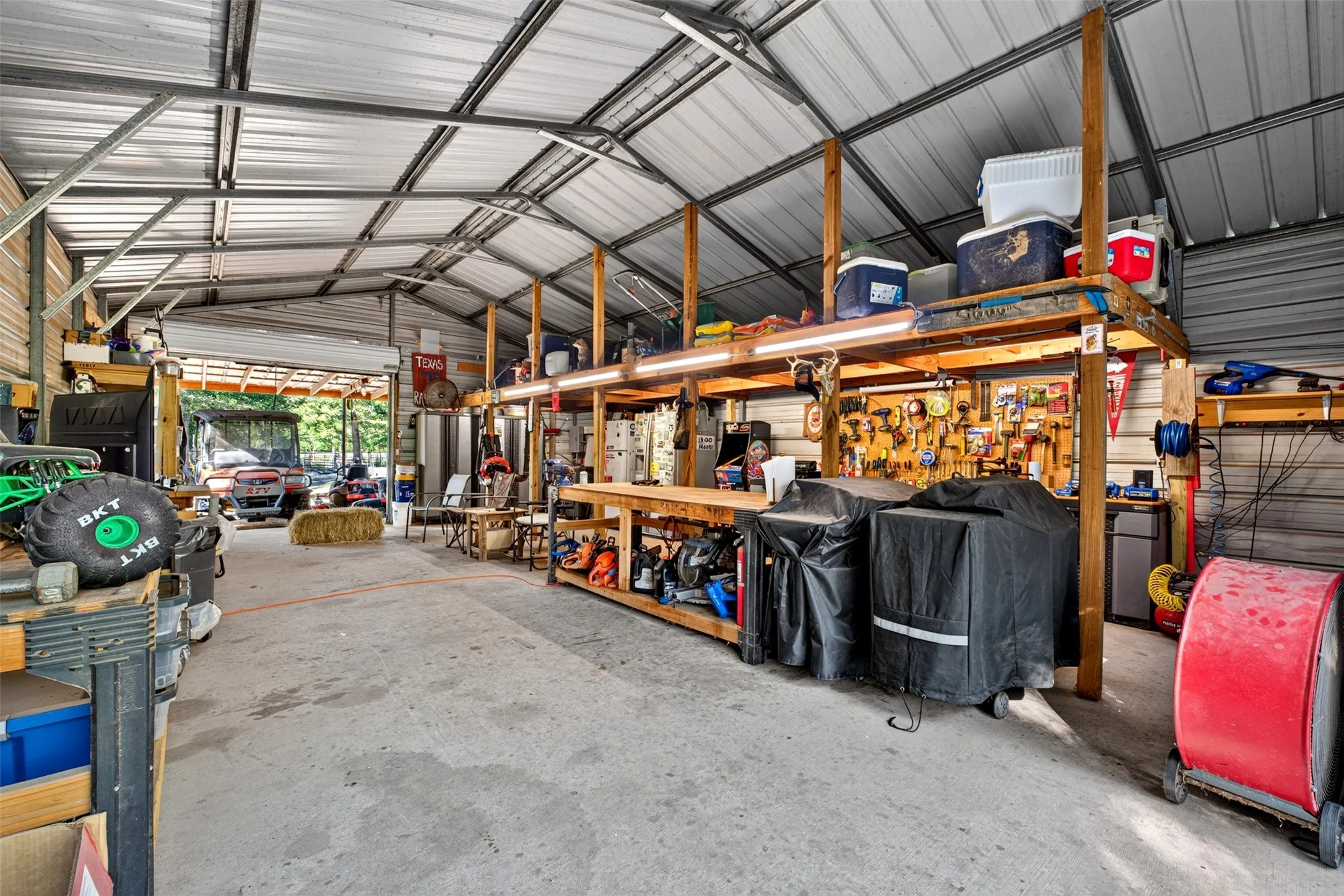 Expansive utility structure featuring a high-pitched metal roof, concrete flooring, and built-in wood shelving