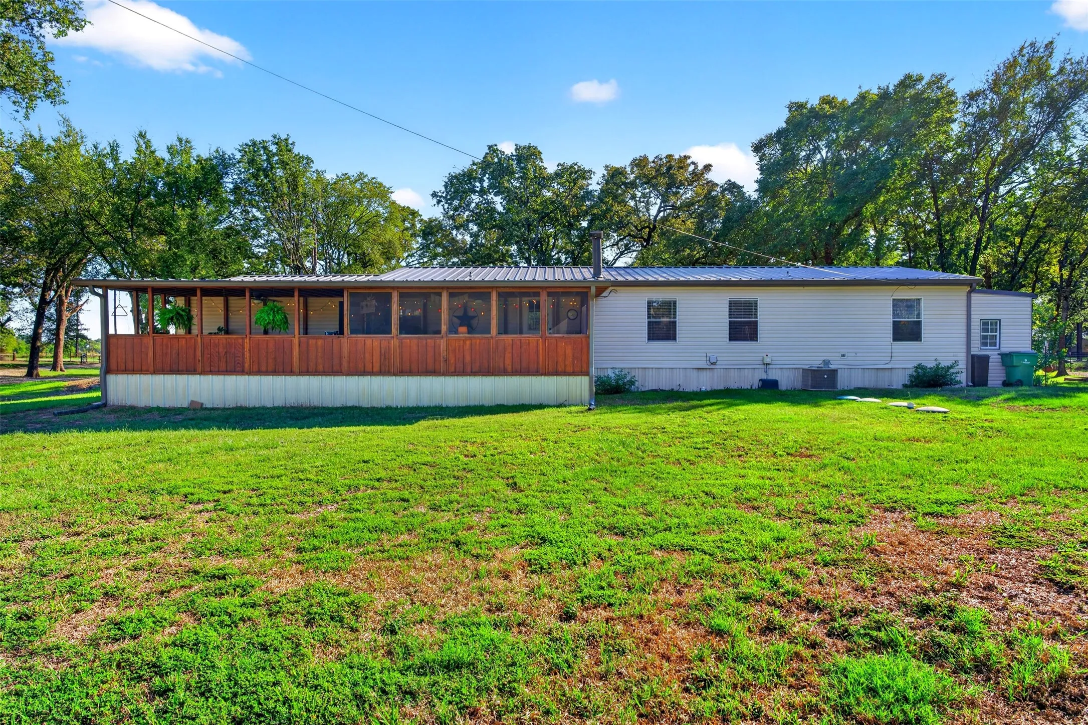 Expansive exterior featuring a screened-in porch with wood-finish siding, a metal roof, and surrounding mature trees