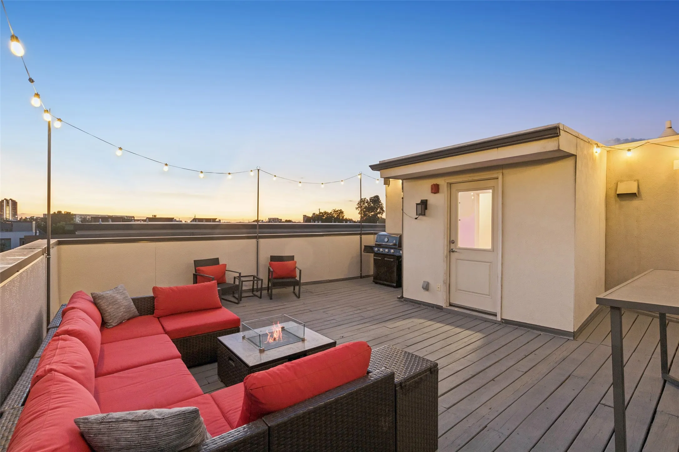 Rooftop deck featuring plank flooring, perimeter string lighting, a built-in fire pit, and a separate structure with an exterior door