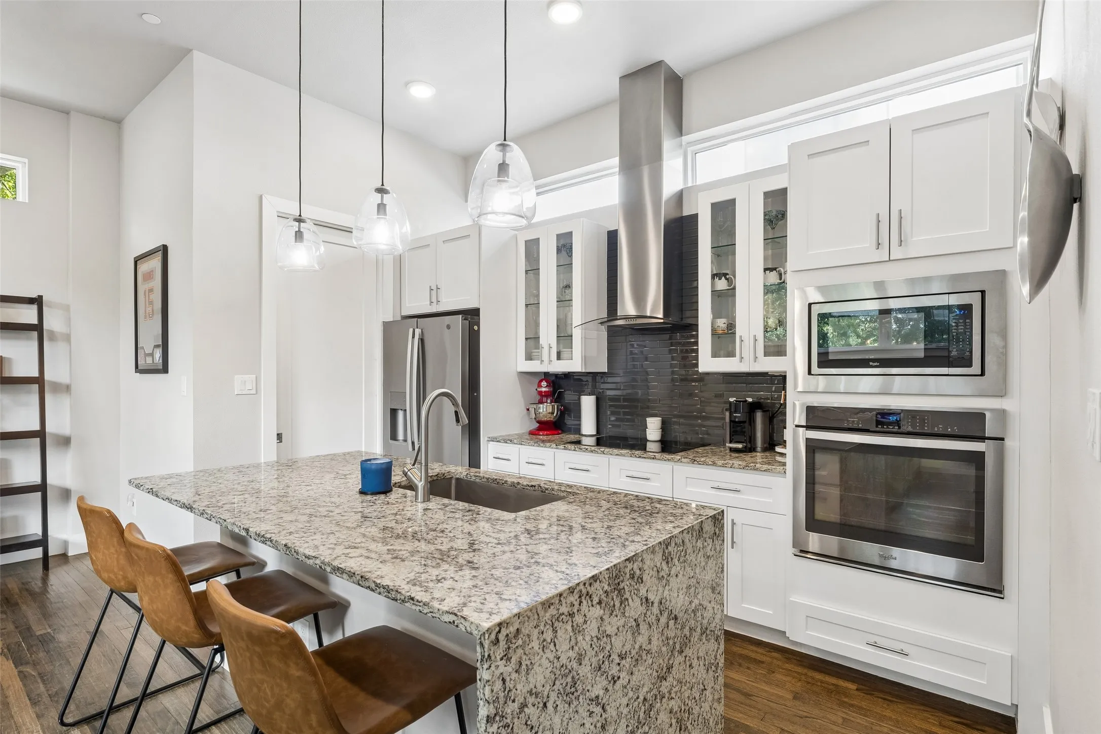 Kitchen featuring white cabinetry, integrated stainless steel appliances, a large island with an undermount sink, and pendant lighting.