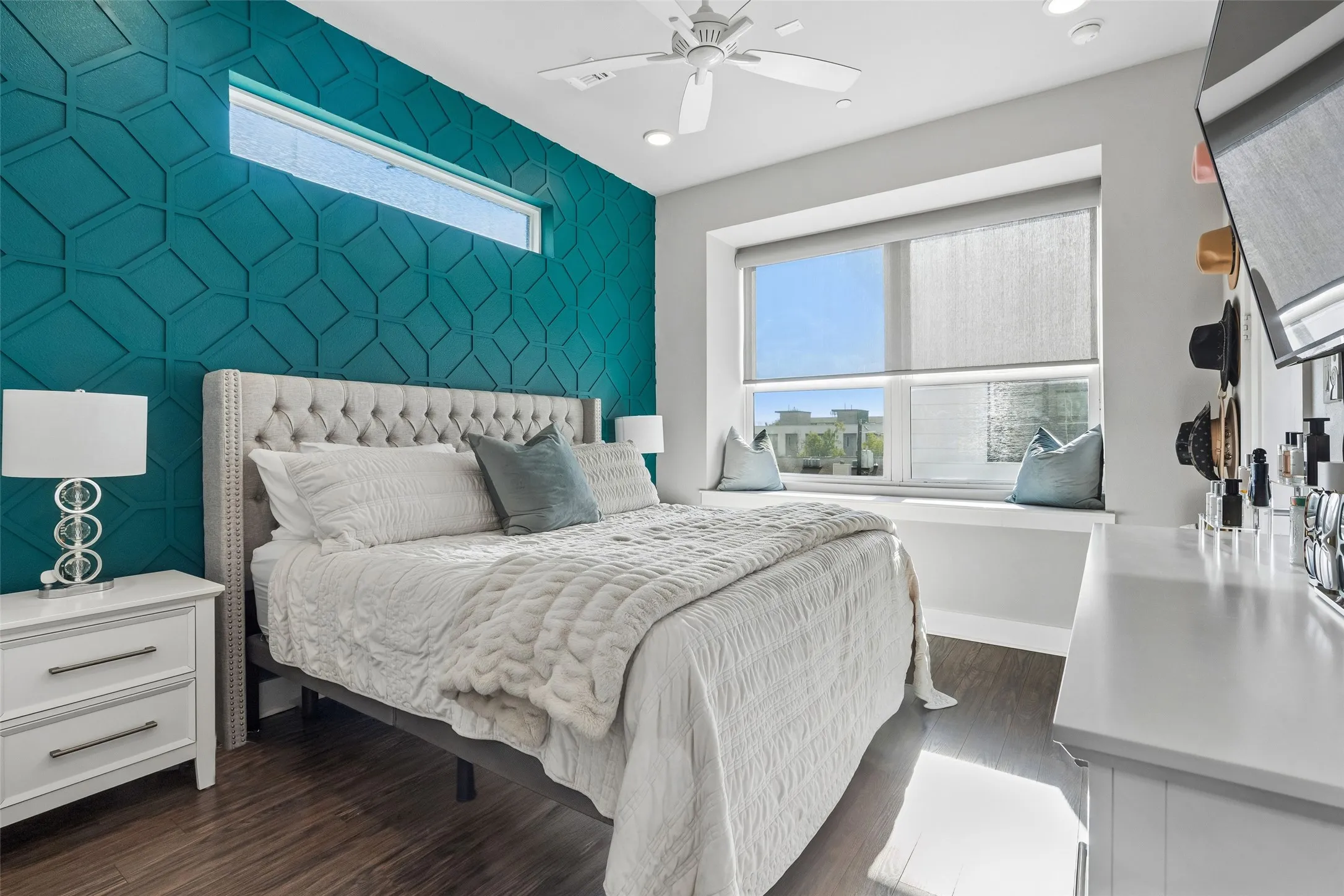 Accent wall with geometric paneling, wood-finish flooring, ceiling fan, transom window, and a window seat with roller shades
