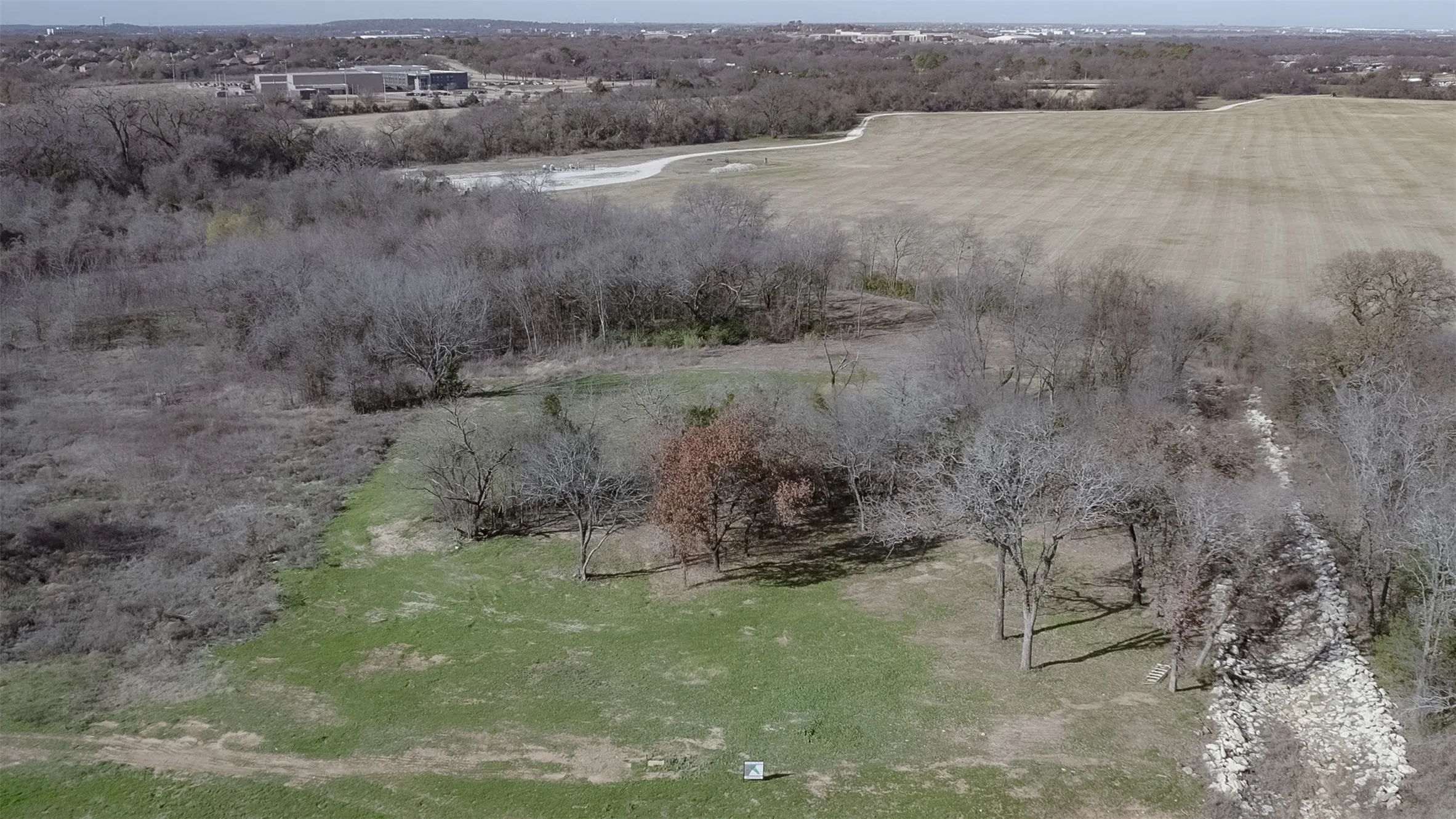 Expansive natural landscape featuring scattered trees, open grassy areas, and distant agricultural fields