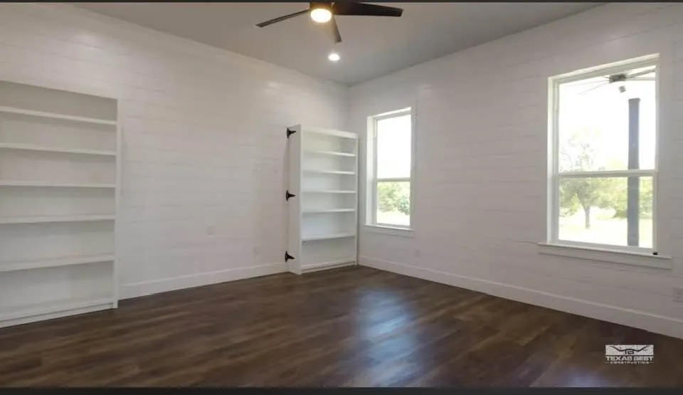 The main-level primary suite is a standout: a spacious 15x16 retreat with a spa-style bath featuring a full-length walk-through glass shower with dual shower heads, a double vanity, and a custom closet — plus a rare bonus, a private 8x12 storm shelter concealed behind built-in bookshelves, complete with its own power, A/C, and ventilation.