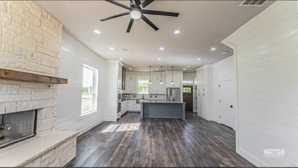 10-foot ceilings and wall-to-wall shiplap set a warm, farmhouse tone over durable luxury vinyl plank flooring. The chef's kitchen anchors an open-concept great room with an oversized Azul Platino granite island, floor-to-ceiling white shaker cabinets, a farmhouse sink, subway tile backsplash, a 5-burner cooktop, and double ovens.