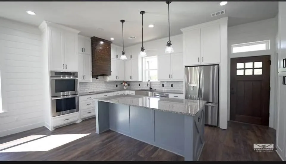 10-foot ceilings and wall-to-wall shiplap set a warm, farmhouse tone over durable luxury vinyl plank flooring. The chef's kitchen anchors an open-concept great room with an oversized Azul Platino granite island, floor-to-ceiling white shaker cabinets, a farmhouse sink, subway tile backsplash, a 5-burner cooktop, and double ovens.