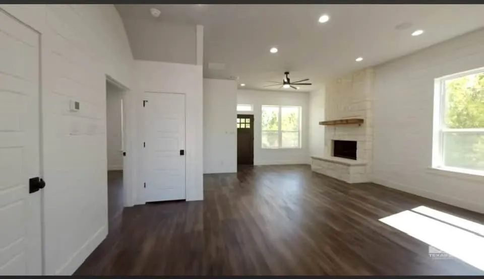 Living area centers on a cozy propane or wood burning fireplace with a cedar mantle and open floor plan. This view is looking to back door to patio.