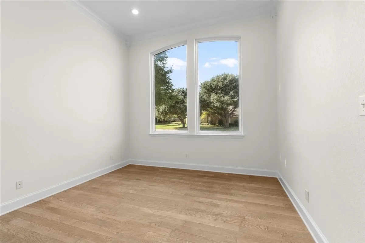 Dual arched windows, wood-finish flooring, recessed ceiling lighting, crown molding, and white wall finishes