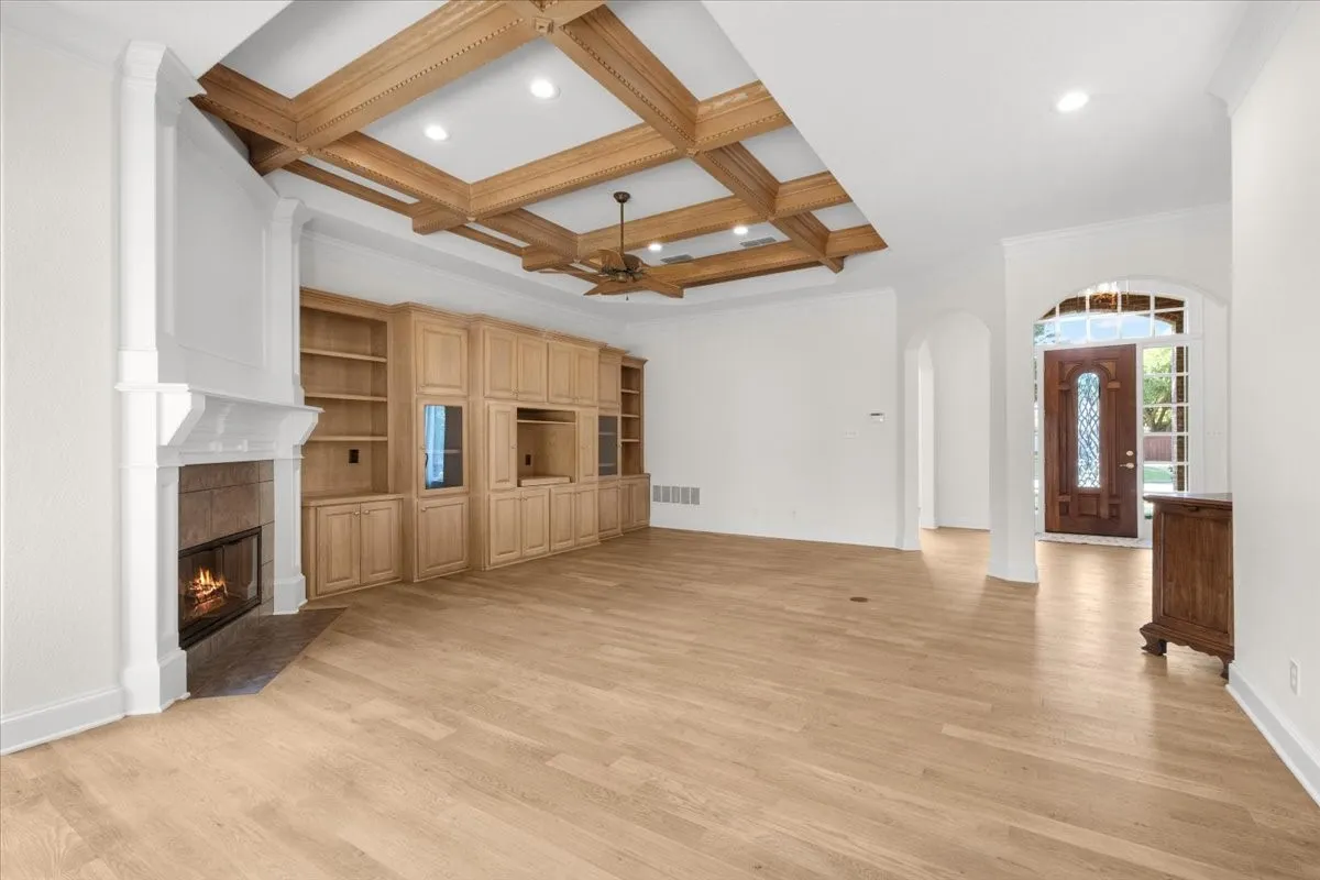 Wood-finish flooring throughout, custom built-in cabinetry, coffered ceiling with recessed lighting, and a detailed fireplace with a substantial mantel