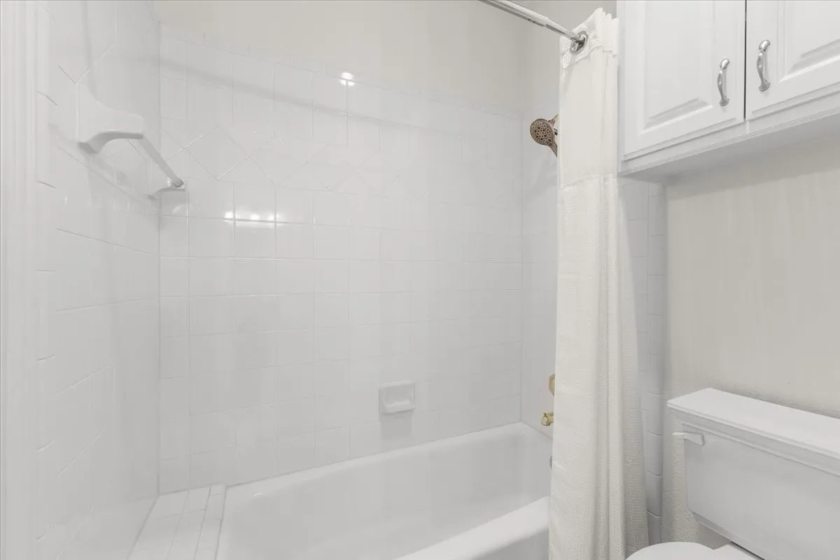 White tiled shower surround, built-in bathtub, shower arm with showerhead, and white cabinetry
