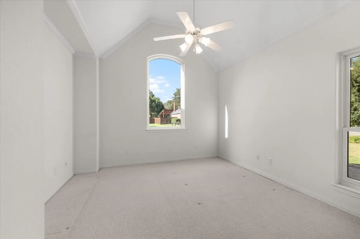 Vaulted ceiling with crown molding, ceiling fan, arched window, and carpeted flooring