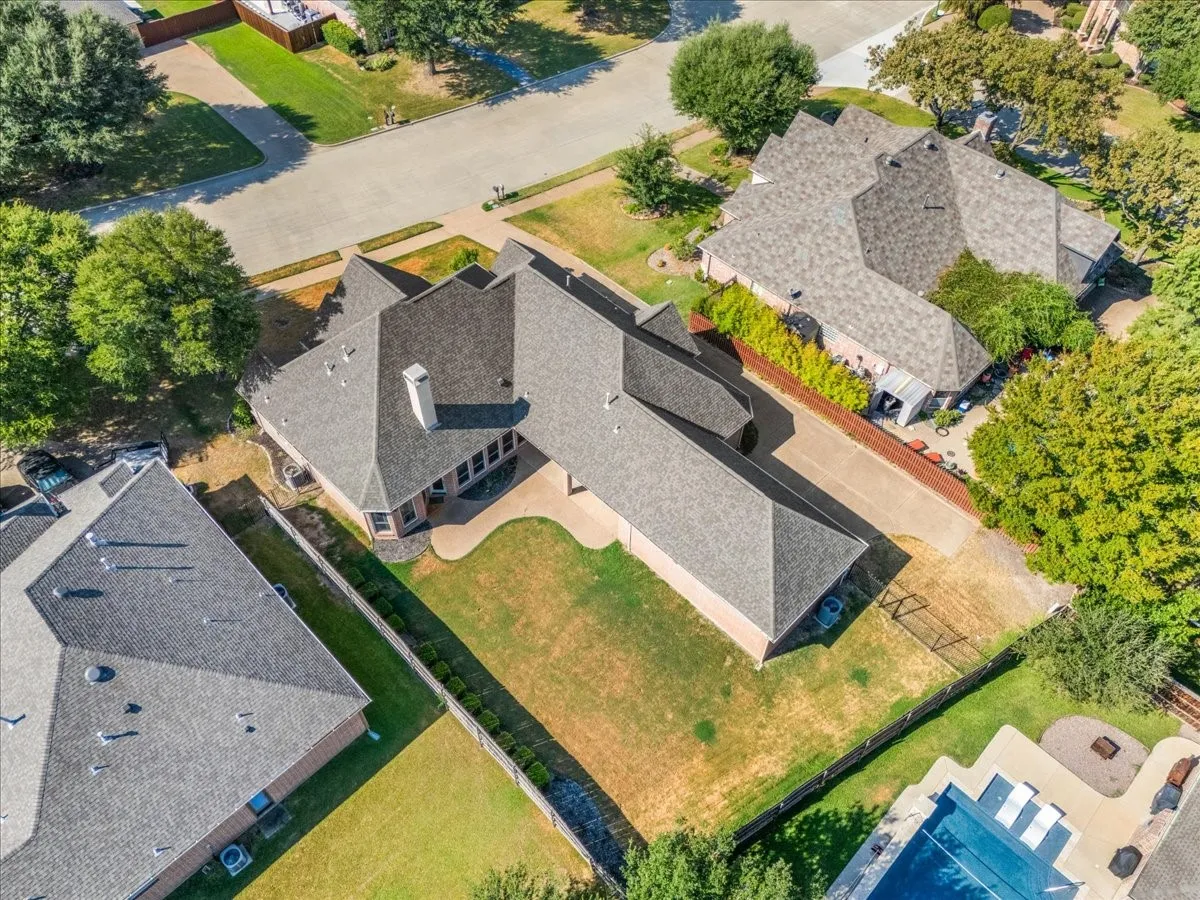 Asphalt shingle roof, chimney, concrete driveway, stone patio, and fenced yard