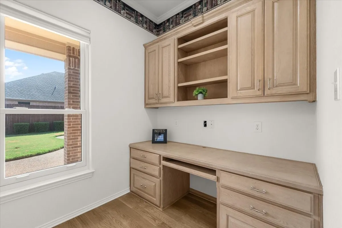 Built-in wood-finish desk with drawers, overhead cabinetry, open shelving, and wood-finish flooring