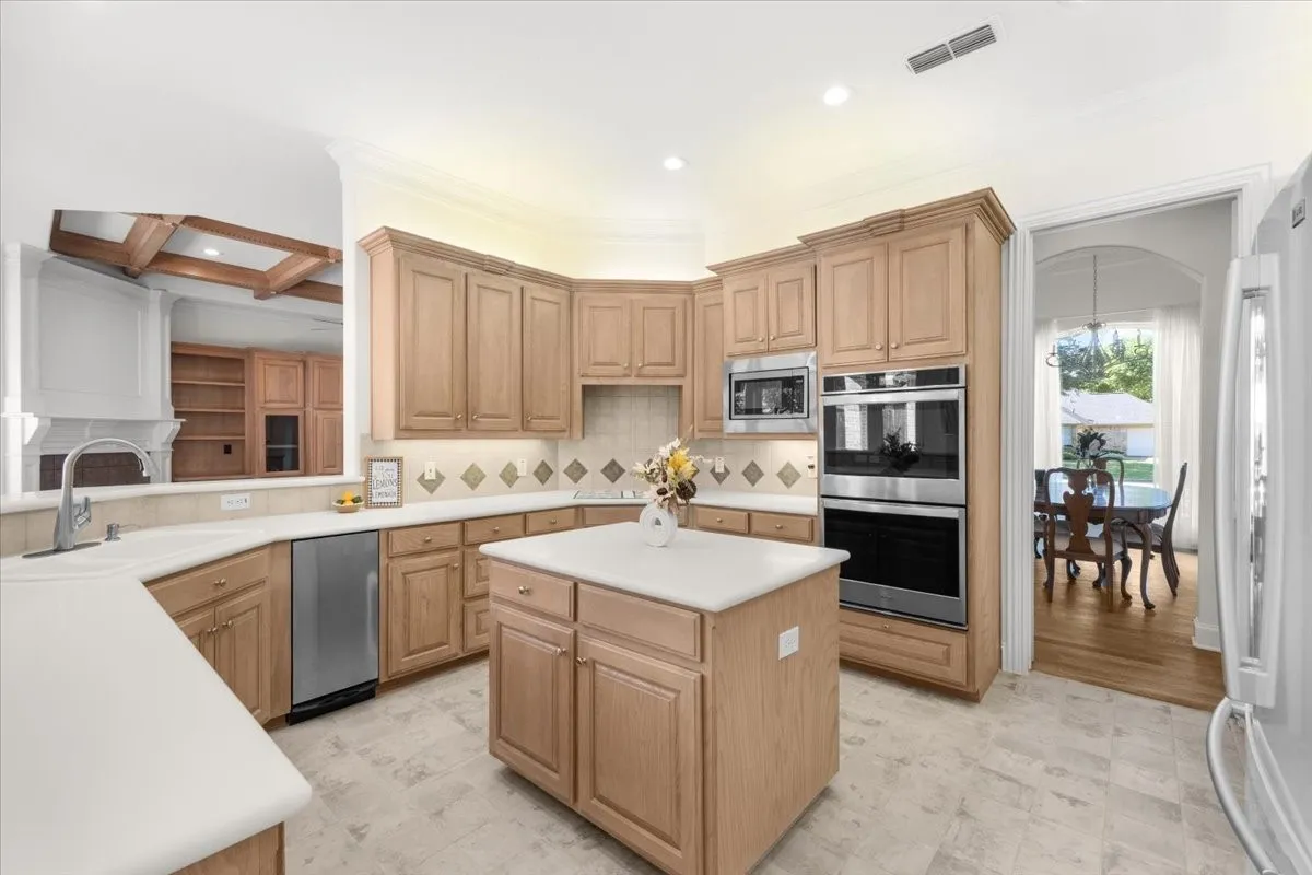 Spacious kitchen featuring warm wood cabinetry, dual wall ovens, stainless steel appliances, and a large center island with white quartz countertop