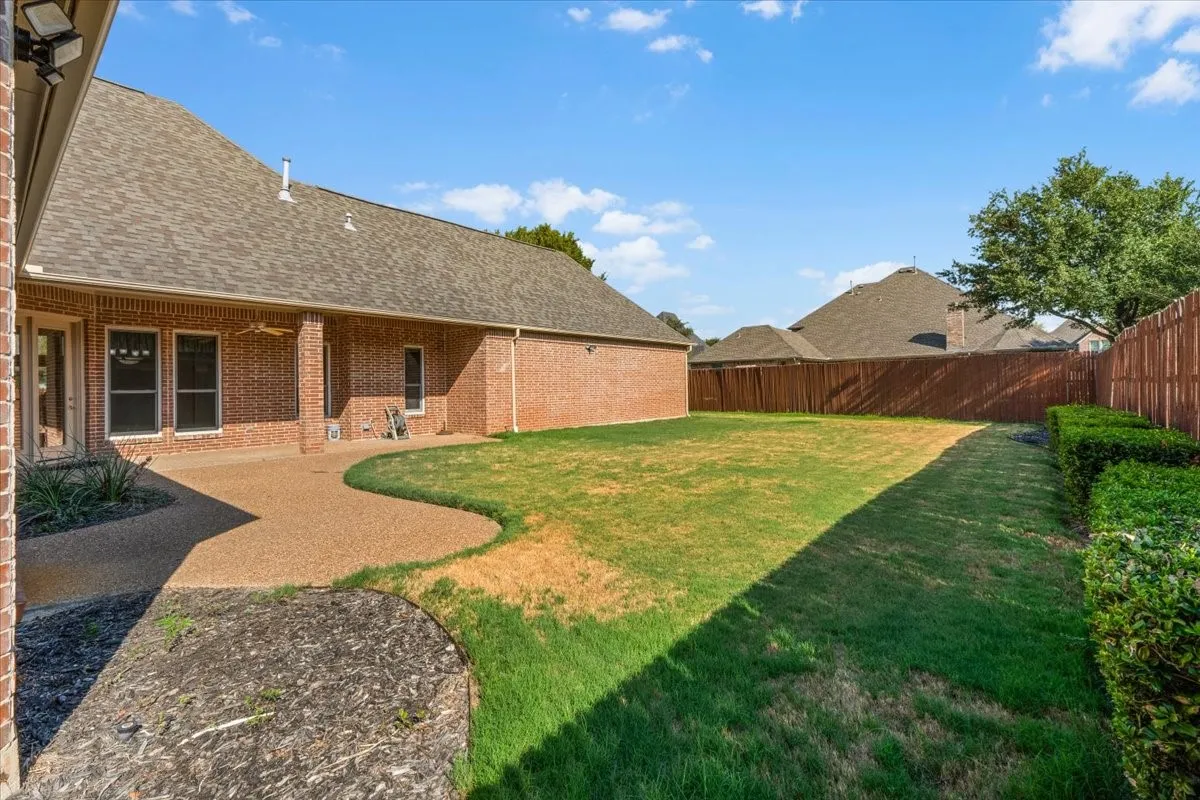 Expansive backyard featuring a red brick exterior, covered patio, gravel-finish concrete pathway, and privacy fencing
