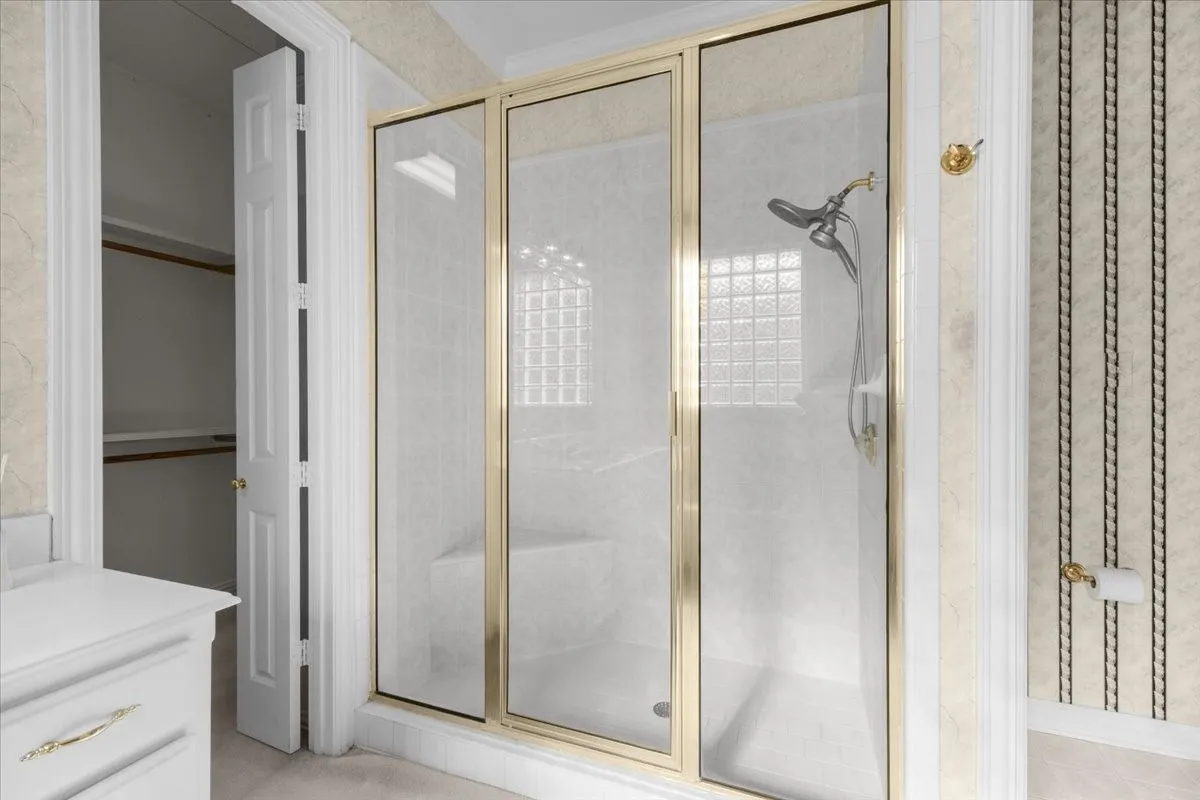 Shower enclosure with gold-finish framing, integrated shower bench, and glass block accent wall