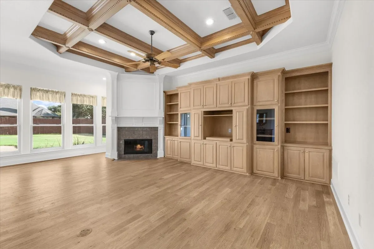 Coffered wood-beam ceiling with an integrated ceiling fan, wood-finish flooring, a stone-faced fireplace with a white mantel, and extensive built-in cabinetry with shelving