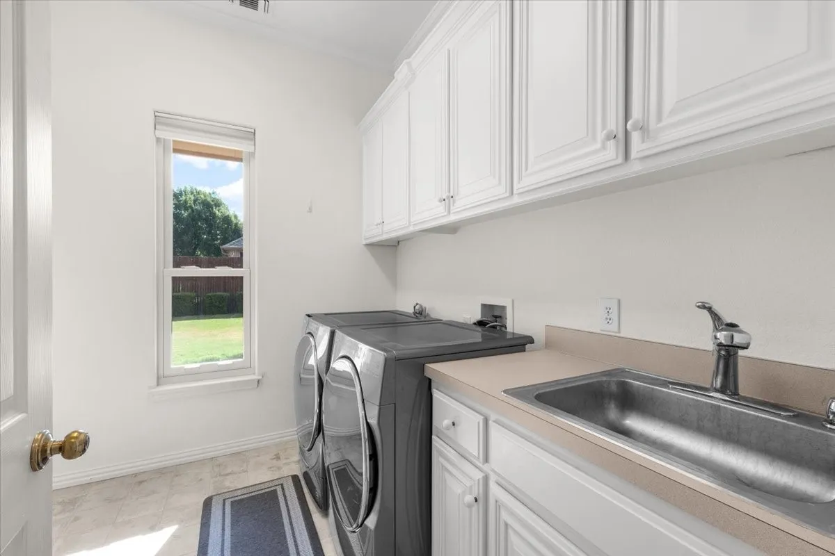 Laundry area featuring upper and lower cabinetry, a stainless steel utility sink, and a window overlooking exterior greenery