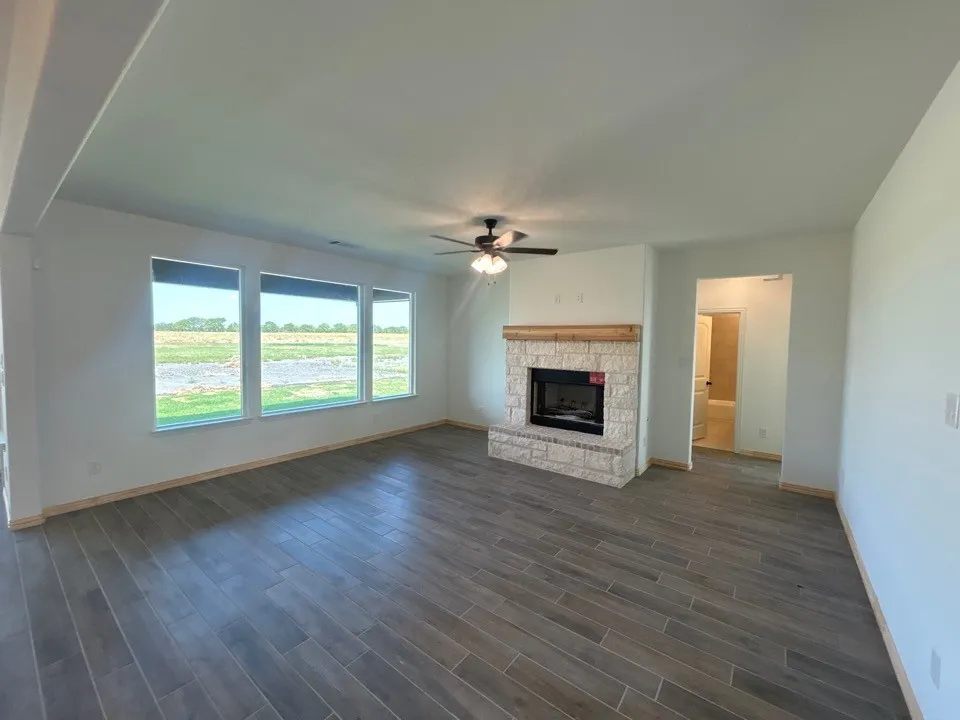 Spacious interior with tile flooring, a stone-front fireplace, a wood mantel, a ceiling fan, and multiple windows