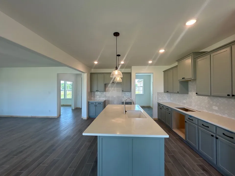 Kitchen with light gray cabinetry, white countertops, textured backsplash, and an island featuring a deep undermount sink and pendant lighting