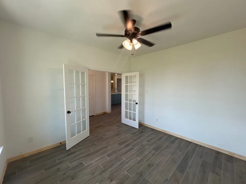 Room featuring wood-finish tile flooring, a ceiling fan with integrated lighting, and white French doors