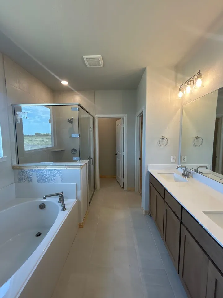 Walk-in shower with glass enclosure, separate soaking tub, dual vanity with solid surface countertop, and large format floor tiling