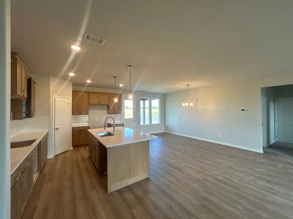Open-concept living area featuring wood-finish flooring, a kitchen island with sink, pendant lighting, and recessed ceiling lights