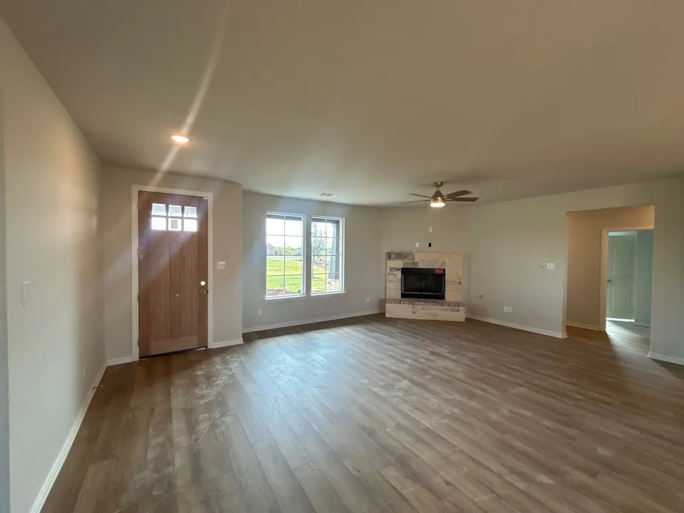 Wood-finish flooring throughout, entry door with clear glass panels, recessed lighting, corner fireplace with tile surround, and an overhead ceiling fan