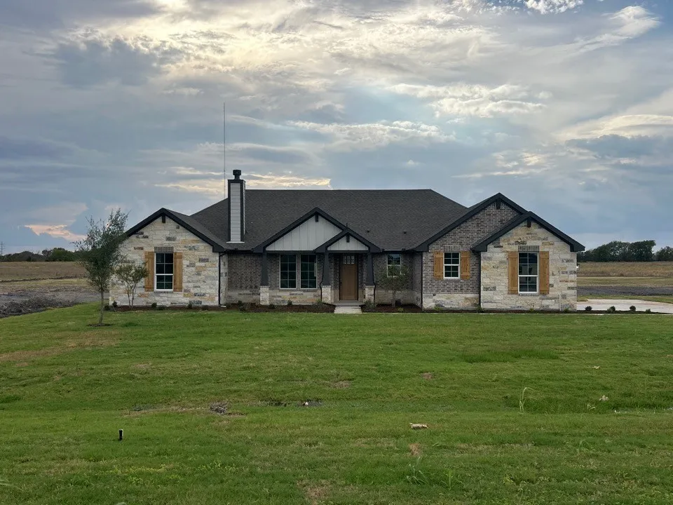 Exterior featuring stone and brick façade, dark shingle roof, wood shutters, and an attached chimney