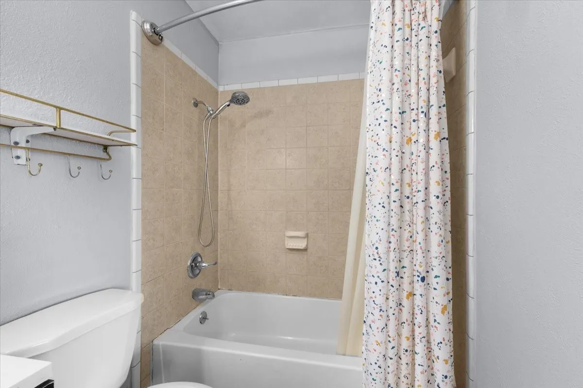 Bathtub with integrated shower, chrome fixtures, and tiled surround