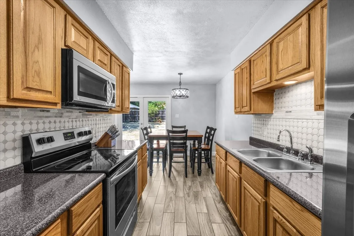 Galley kitchen featuring wood cabinetry, stainless steel appliances, speckled countertops, and a full tile backsplash