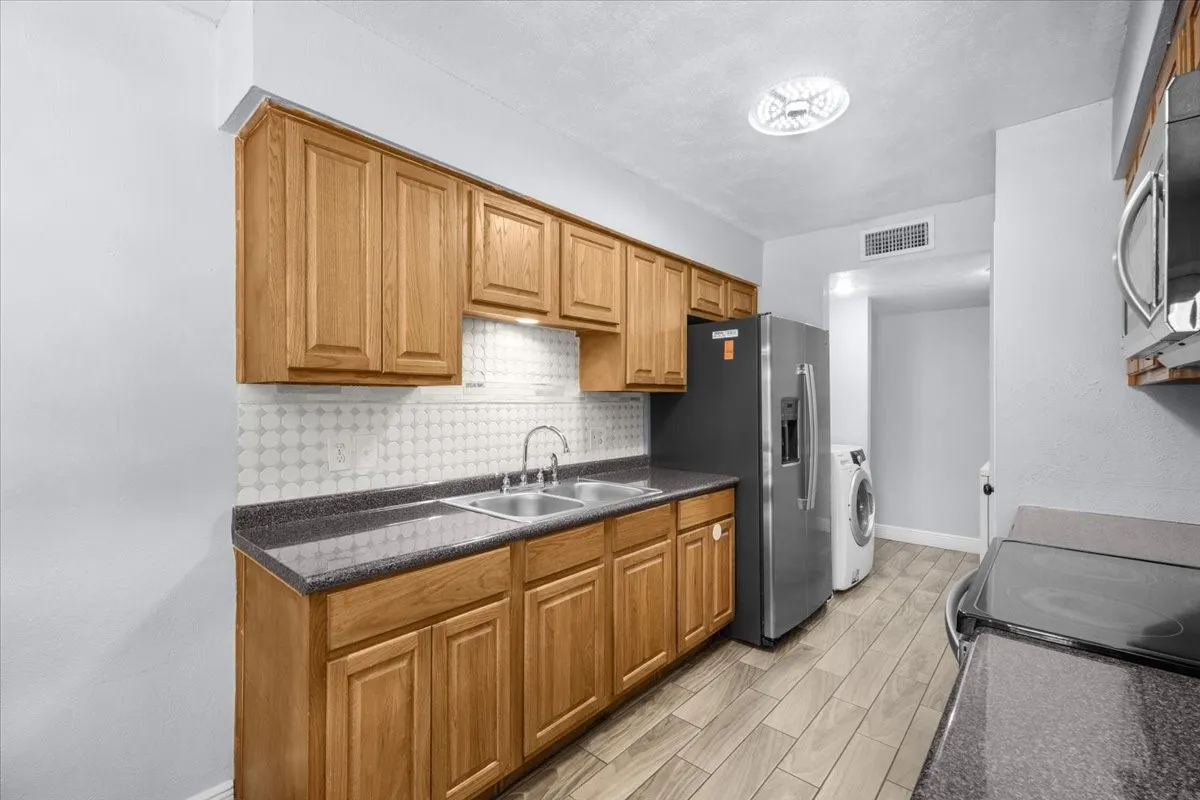 Kitchen featuring wood cabinetry, stainless steel sink, patterned tile backsplash, and light wood-finish flooring