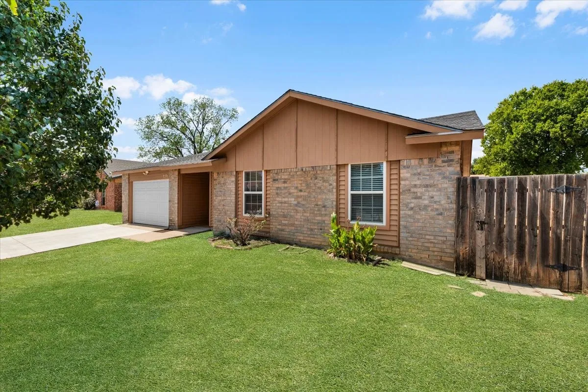 Brick and siding exterior with a pitched roof, attached garage with a white door, and a wooden privacy fence