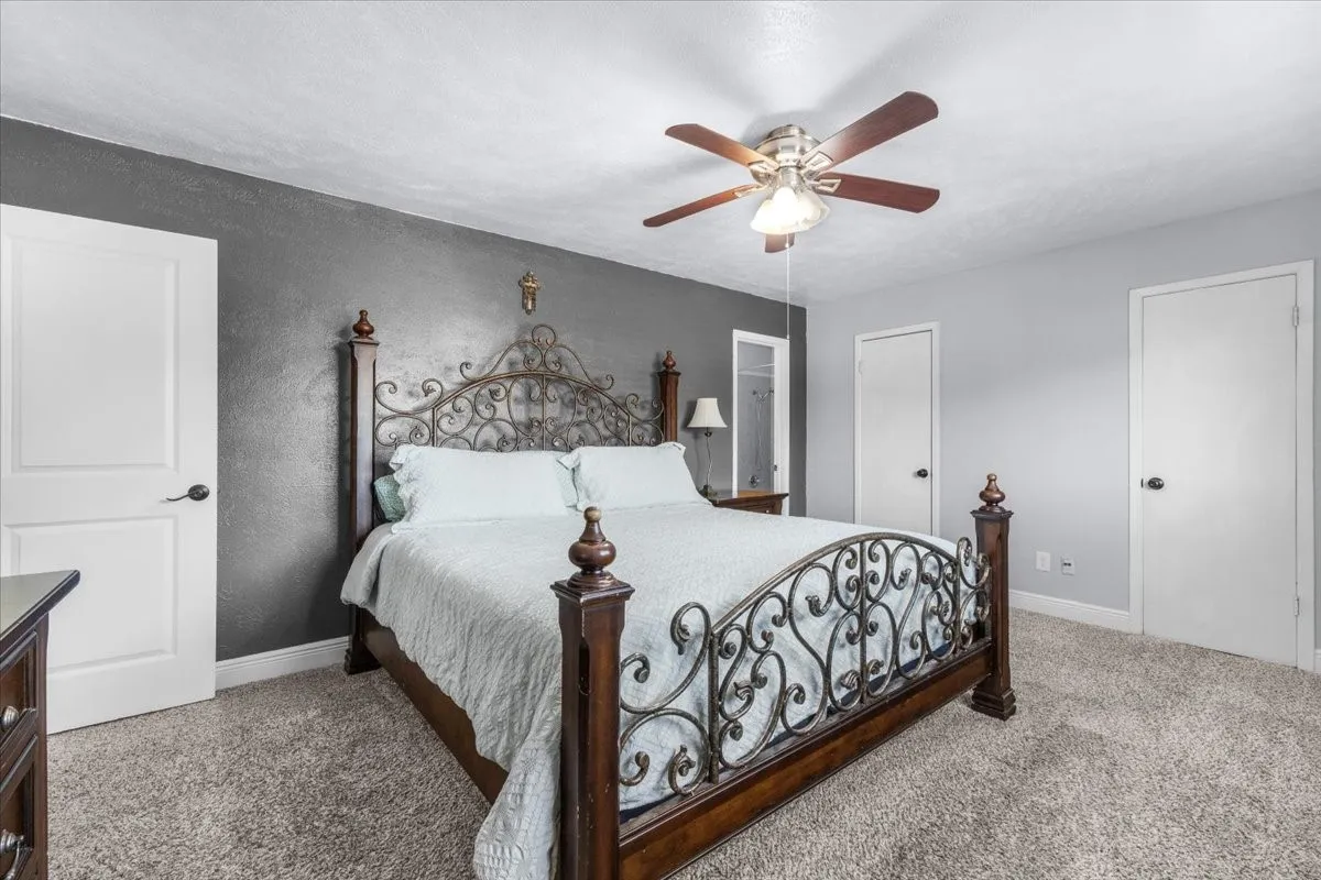Plush carpet flooring, ceiling fan with integrated lighting, two-panel interior doors, and textured walls