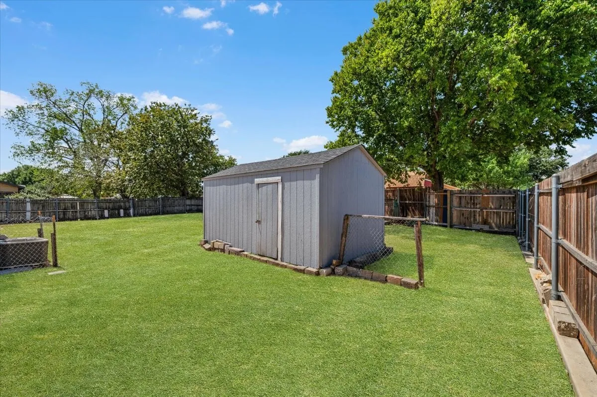 Expansive backyard featuring a manicured lawn, a storage shed, and mature trees