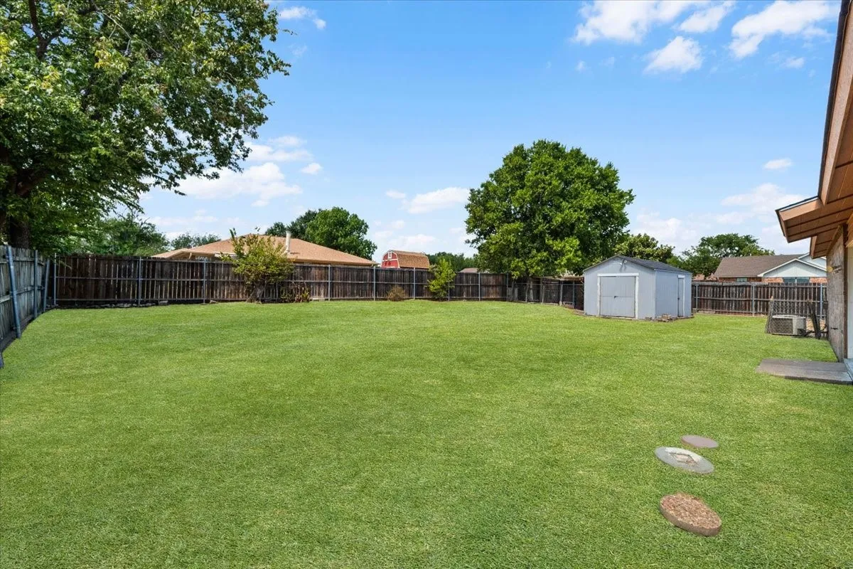 Expansive backyard featuring a lush lawn, privacy fencing, a storage shed, and mature trees